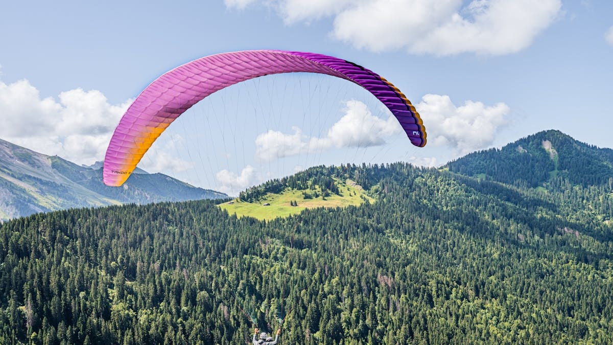 Experience an adventurous paragliding flight over lush alpine landscapes under a vibrant sky.